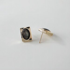 May include: A pair of gold-toned earrings with black oval-shaped stones set in square frames.