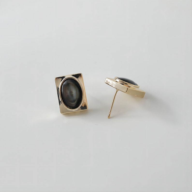 May include: A pair of gold-toned earrings with black oval-shaped stones set in square frames.