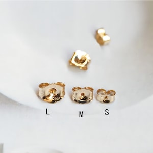 Puede incluir: Tres respaldos de pendientes de oro en diferentes tamaños: grande, mediano y pequeño. Los respaldos son de metal y tienen un acabado liso.