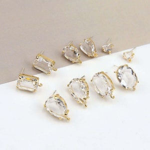 May include: Assortment of clear crystal earring components with gold-toned settings and jump rings. The crystals are in various shapes, including teardrop, oval, and rectangular.