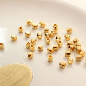 Może przedstawiać: Zbiór złotych metalowych koralików, każdy o sześciokątnym kształcie. Koraliki są rozrzucone na białej powierzchni.