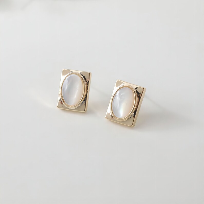 May include: A pair of gold earrings with oval-shaped white stones set in square frames.