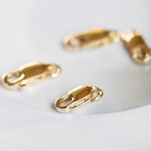 May include: Four gold-toned metal lobster clasps, commonly used for jewelry making.