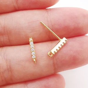 May include: Two gold earring findings, one with a straight bar and clear cubic zirconia stones, the other with a sawtooth edge.