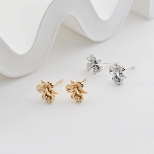 Könnte beinhalten: Ein Paar Ohrstecker in Form von Blumen, einer in Gold und der andere in Silber, mit einem kleinen, klaren Stein in der Mitte jeder Blume.