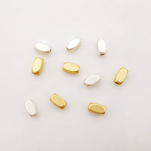 Könnte beinhalten: Eine Sammlung von goldenen und silbernen Metallperlen, perfekt für die Schmuckherstellung. Die Perlen sind oval geformt und haben eine glatte, polierte Oberfläche.