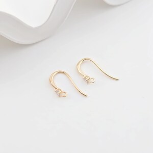 May include: A pair of gold-tone earring hooks with a small clear crystal at the top of each hook.