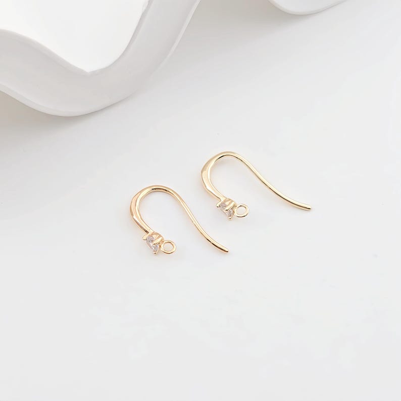 May include: A pair of gold-tone earring hooks with a small clear crystal at the top of each hook.