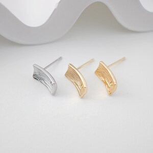 Pode incluir: Dois pares de brincos, um prateado e outro dourado, com formato retangular texturizado. Os brincos são simples e elegantes.