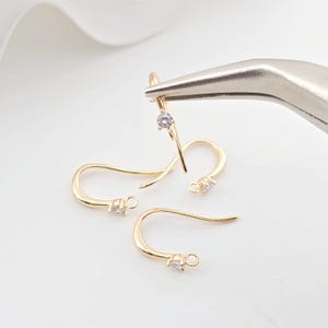May include: Three gold-toned earring hooks with a small clear rhinestone at the top of each hook.