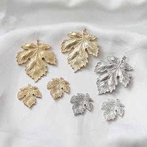 May include: A collection of seven metal leaf charms in varying sizes, featuring detailed veining and textures. The set includes four gold-toned leaf pendants and three silver-toned leaf pendants, each with a small loop at the top for attachment.