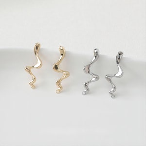 May include: A pair of gold and silver earrings with a wavy, abstract design. The earrings are made of metal and have a simple, modern style.