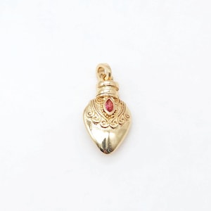 May include: A gold heart-shaped pendant with a red gemstone in the center. The pendant has intricate details and a loop at the top for attaching to a chain.