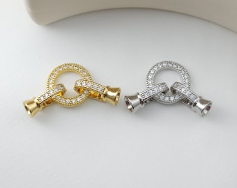 May include: Two metal clasps with a circle design, one gold and one silver, both adorned with clear cubic zirconia stones.