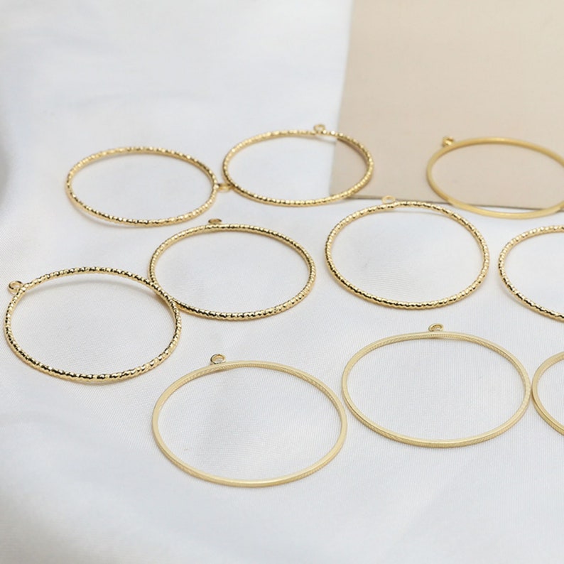 May include: A set of ten gold-toned metal hoops with a textured surface. The hoops are of varying sizes and have a small loop at the top.