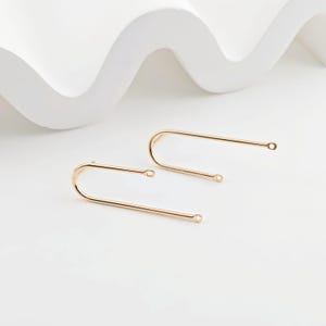 Op de afbeelding: Een paar gouden oorbelbevestigingen met een lus aan het ene uiteinde en een kleine springring aan het andere uiteinde.