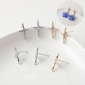 Pode incluir: Seis fechos de brincos de prata e ouro com um design de estrela. Os fechos têm um pequeno laço na parte inferior e um poste na parte de trás. O design da estrela tem um pequeno strass transparente no centro.