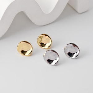 May include: Four irregularly shaped stud earrings. Two are gold-toned, and two are silver-toned. The earrings have a smooth, reflective surface and a slightly organic, pebble-like design. They are displayed on a white surface.