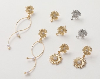 Könnte beinhalten: Eine Auswahl an gold- und silberfarbenen Ohrringen in Form von Gänseblümchen. Einige haben ein hängendes Design mit Perlen. Die Gänseblümchen-Mittelstücke sind mit kleinen, klaren Kristallen verziert. Die Ohrringe werden auf einer weißen Oberfläche präsentiert.