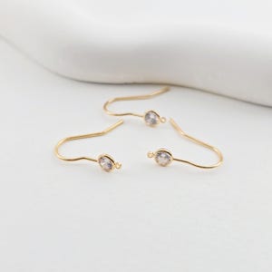 May include: Two gold earring hooks with clear round stones attached to the end of each hook.