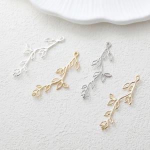 May include: Four metal jewellery charms shaped like delicate leafy branches. Two charms have a bright silver finish, and two charms have a warm gold finish. Each charm features a slender stem with multiple small, open-work leaf shapes attached.