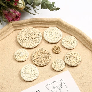 May include: A selection of woven rattan coasters in different sizes. The circular coasters have a natural beige hue and a textured surface. They are displayed on a light brown tray, with dried flowers visible in the background.