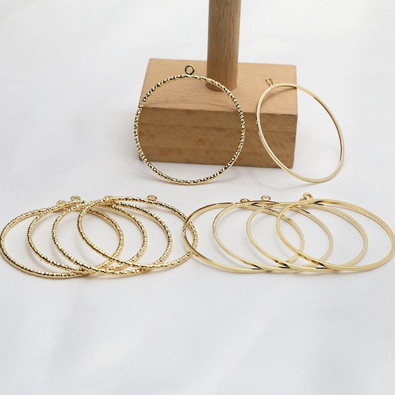 May include: A set of gold-toned metal hoops, some with a textured finish, and some smooth. The hoops are of varying sizes and are arranged in a semi-circle.
