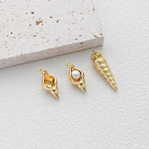 May include: Three gold-colored seashell charms. Two charms have a shell shape, one with a pearl inside. The third charm is a long, spiraled shell. All charms have a loop for attaching to jewelry.