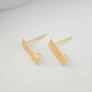 May include: Two gold-toned earring blanks with a textured finish. Each blank has a rectangular shape with a small loop at the bottom.