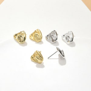 Puede incluir: Un conjunto de cuatro pendientes con un diseño de gesto de mano. Dos pendientes son de oro y dos son de plata.