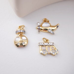 May include: Three gold-tone charms with white enamel and clear rhinestones. The charms are shaped like a plane, a bus, and a cable car.