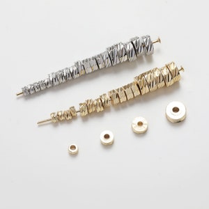 May include: A set of gold and silver metal beads with a textured, twisted design. The beads are arranged in size order, with the smallest beads at the bottom and the largest beads at the top. There are also several plain metal rings of varying sizes.