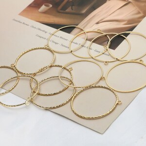 May include: A set of ten gold-toned metal hoops with a textured surface. The hoops are of varying sizes and are arranged in a random pattern.