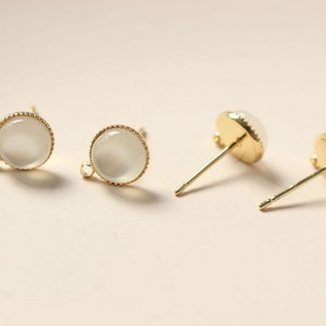May include: A pair of gold-tone earring studs with white round cabochon stones.