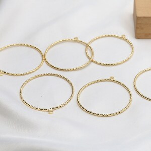 May include: Six gold-toned metal hoops with a textured surface. The hoops have a small jump ring on one side.