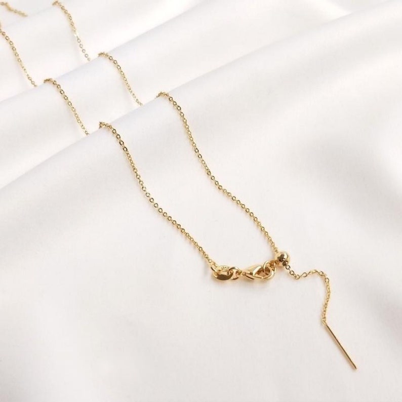 Peut inclure: Un collier en cha&icirc;ne dor&eacute;e avec un fermoir coulissant et une petite perle &agrave; l'extr&eacute;mit&eacute;. La cha&icirc;ne est d&eacute;licate et a un &eacute;clat subtil.