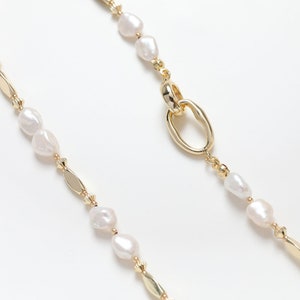 May include: A gold chain necklace with white pearl beads and a gold oval link.