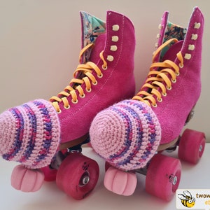 May include: Pair of vibrant pink roller skates with yellow laces and pink wheels. The skates feature a floral lining and are accessorized with striped crochet toe caps in pink and purple hues.