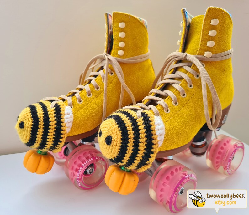 May include: A pair of yellow roller skates with tan laces and black and yellow crocheted bee-themed toe caps. The wheels are pink and the toe stops are orange. The skates have a suede-like texture. The Etsy shop logo is in the bottom right corner.
