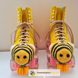 May include: A pair of yellow roller skates with tan laces and pink wheels. Each skate has a crocheted bee design on the toe and a small orange pumpkin attached. The skates are from two woolly bees etsy dot com.