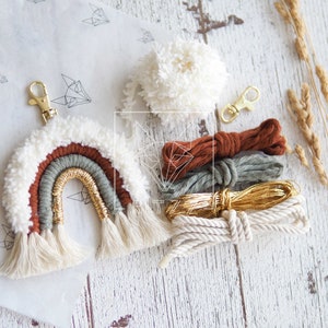 May include: A DIY kit for making a rainbow macrame keychain. The kit includes white, brown, green, and gold yarn, a white pom-pom, and a gold key ring.
