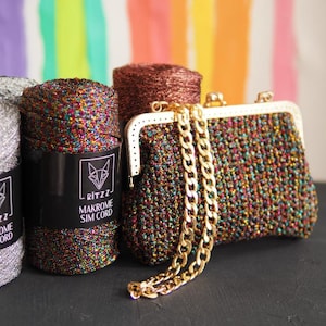 May include: Three spools of colourful, sparkly macrame cord with the brand name "RITZ2 MAKROME SIM CORD" printed on the labels. A small, crocheted purse with a gold chain strap is in the foreground.