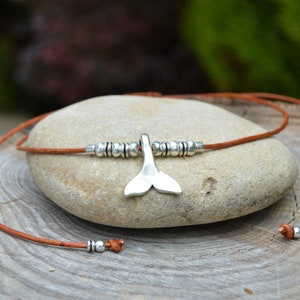 Può includere: Una collana in corda di cuoio marrone con un ciondolo a forma di coda di balena argentata e perline argentate.