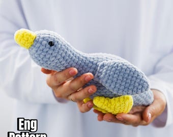 May include: A crocheted blue duck with a yellow beak and feet. The duck is being held in someone's hands. The text "Eng Pattern" is visible in the bottom left corner of the image.