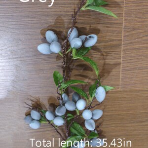 May include: A branch of artificial grey berries with green leaves. The branch is approximately 35.43 inches long.  Grey.