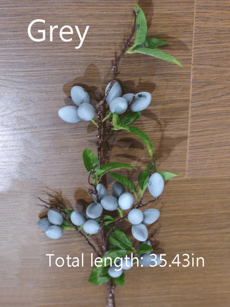 May include: A branch of artificial grey berries with green leaves. The branch is approximately 35.43 inches long.  Grey.