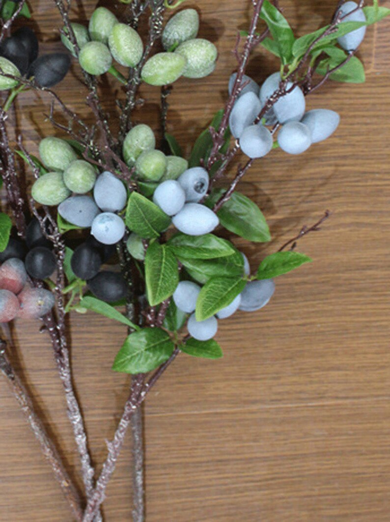 May include: A bunch of artificial green and blue berries on brown twigs with green leaves. The berries are clustered together and look realistic.