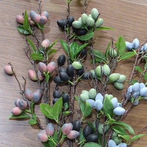 May include: A bunch of artificial berry sprigs with green leaves. The berries are in shades of blue, green, pink, and black.