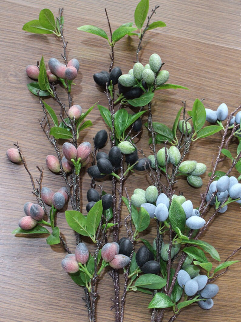 May include: A bunch of artificial berry sprigs with green leaves. The berries are in shades of blue, green, pink, and black.
