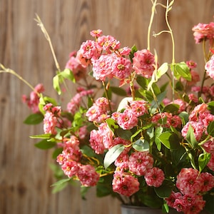 May include: A bouquet of pink artificial flowers with green leaves. The flowers are clustered together and have a delicate, ruffled appearance.